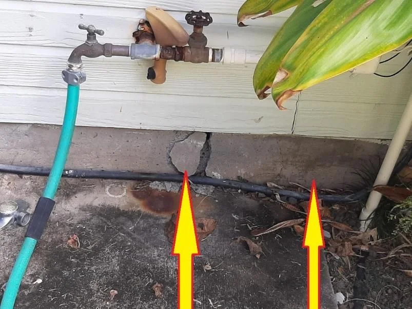 Arrows highlight cracks in a concrete foundation below an outdoor faucet.